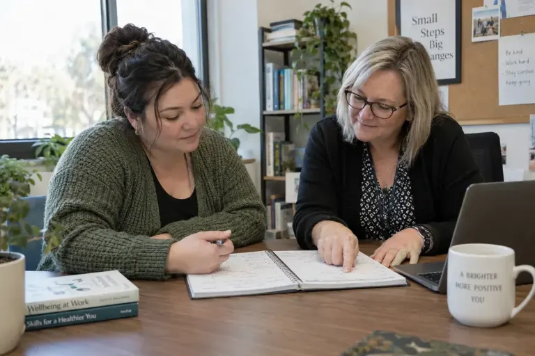 Adult discussing a weekly work schedule with a supportive adviser at a quiet office table, calendar with small indistinct writing.